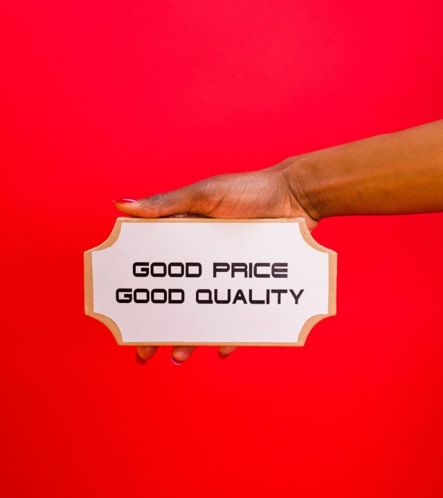 A hand holding a sign with 'Good Price, Good Quality' text against a bright red background.